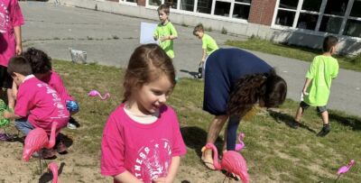 A girl in a pink shirt looking over some pink plastic flamingos in the playground among her friends.