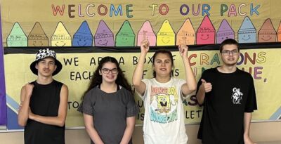 A group of teens in front of a welcome sign in their classroom.